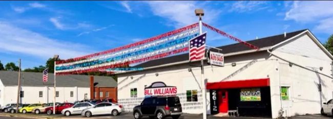 Front view of a car dealership with red, white, and blue bunting and a U.S. flag on the roof