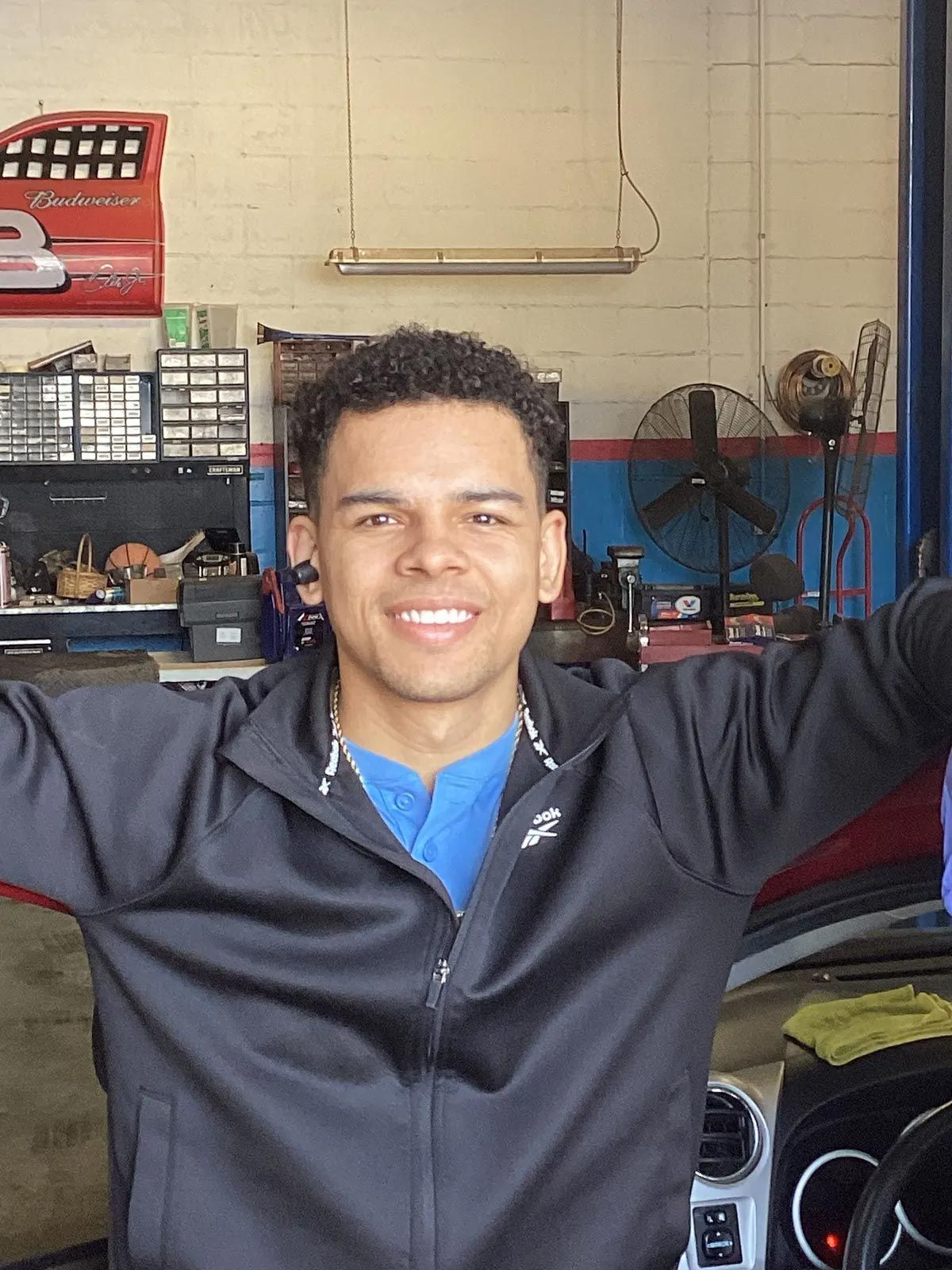Person smiling with arms raised in a garage or workshop, with tools and equipment in the background.