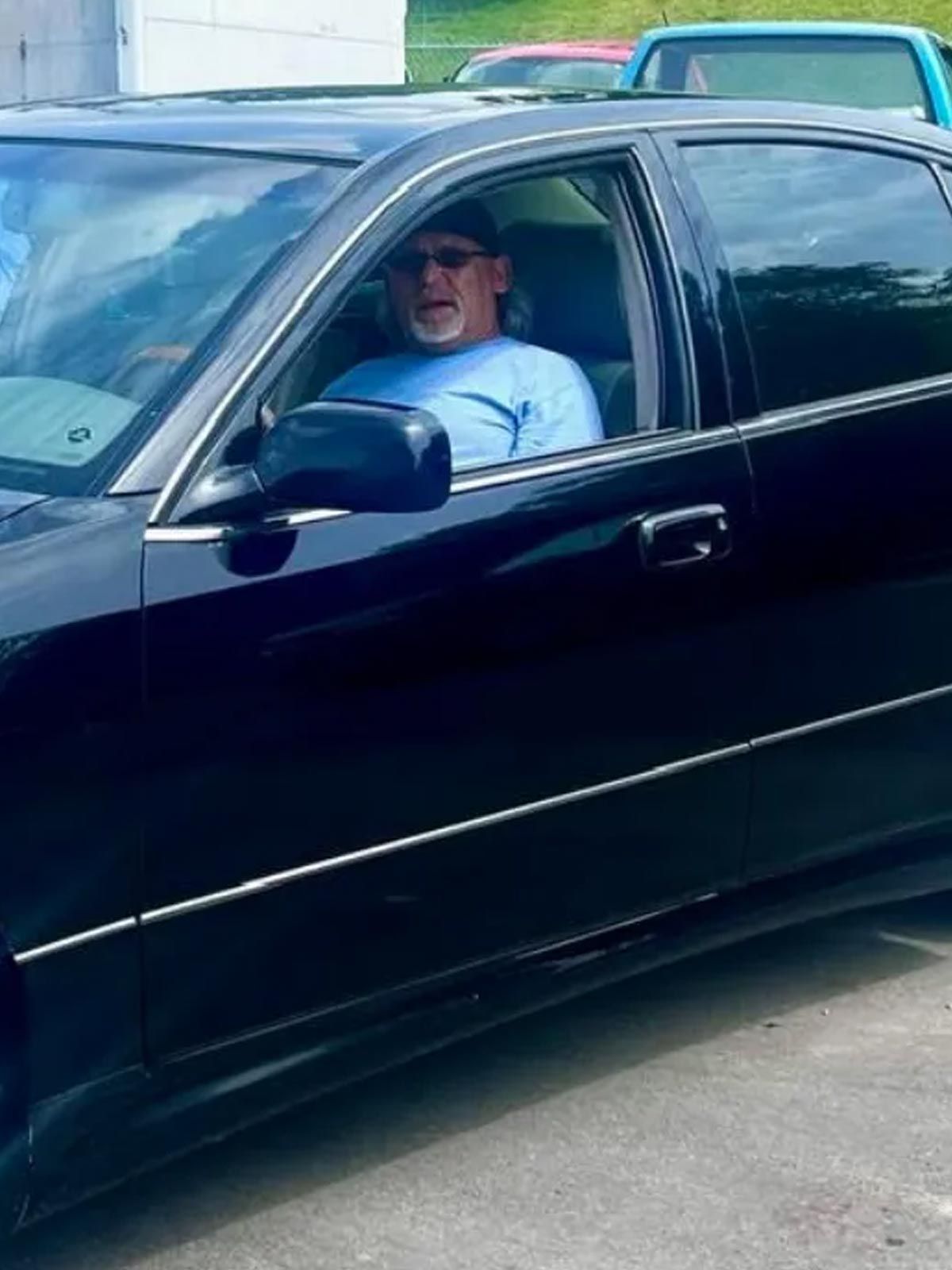 Driver sitting in a black car with the window down in a parking lot