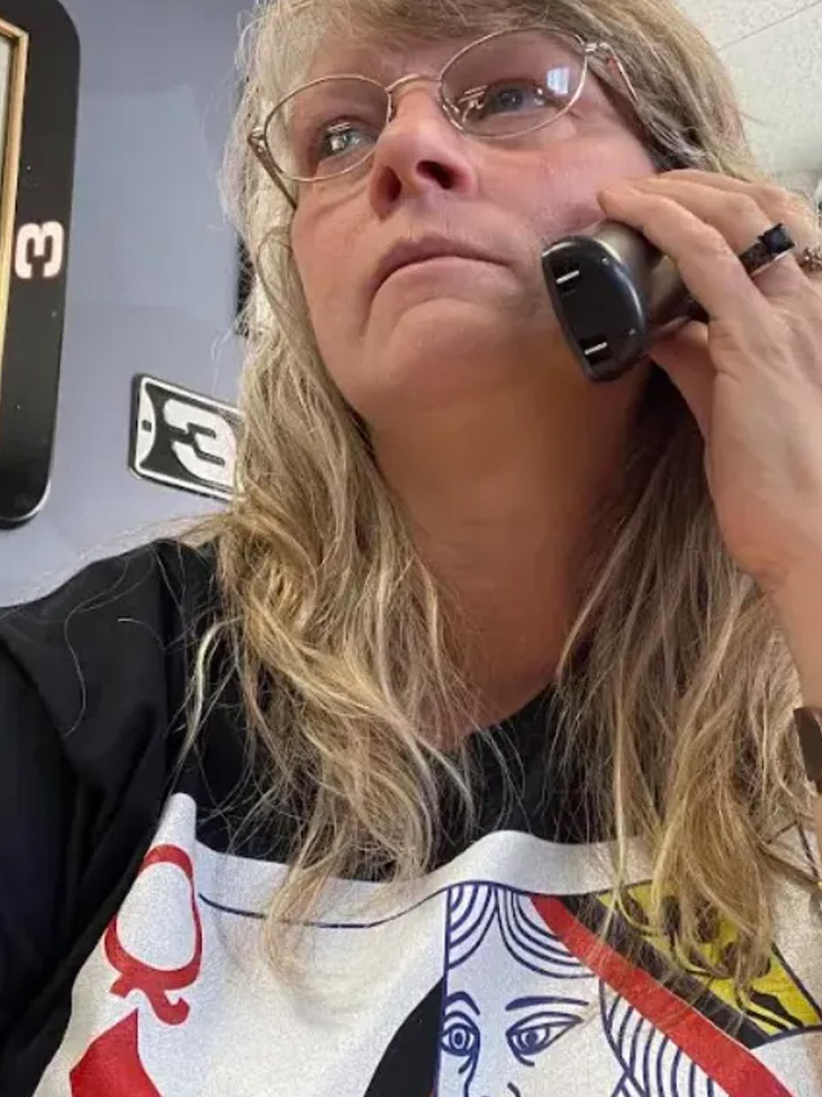Close-up of a person in glasses holding a phone to their ear, wearing a black graphic T-shirt.