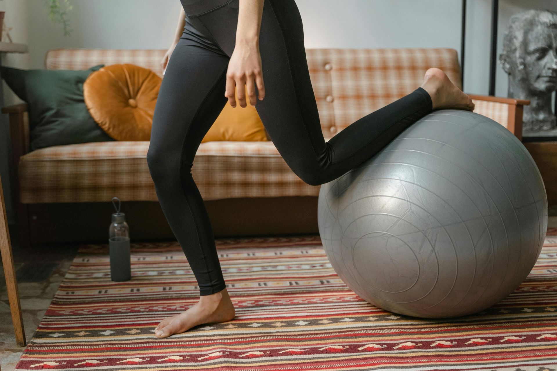 Person doing a lunge with one foot on a stability ball, indoors, with a couch in the background.