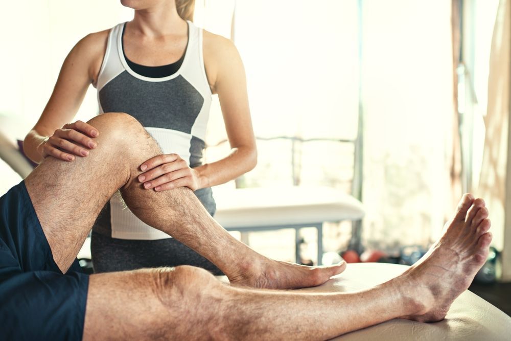 A physical therapist performs an examination on a patient's knee in a clinical setting.