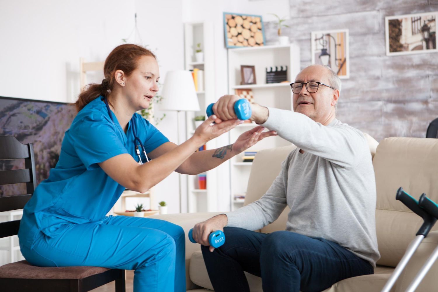 Woman in blue uniform assisting a person lifting dumbbells indoors. Crutches on the side.