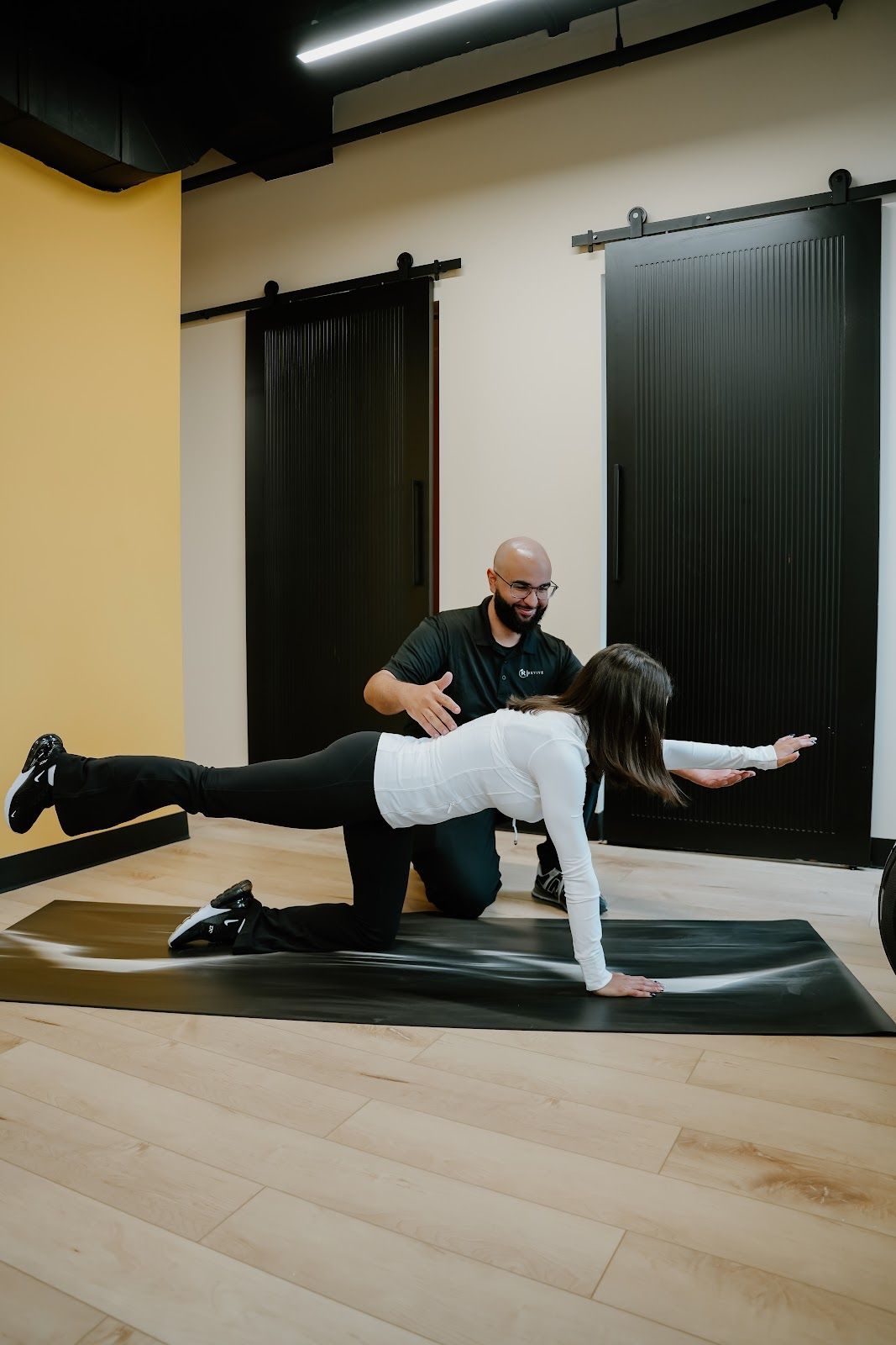 Person doing a balancing exercise on a mat with a coach in a gym.
