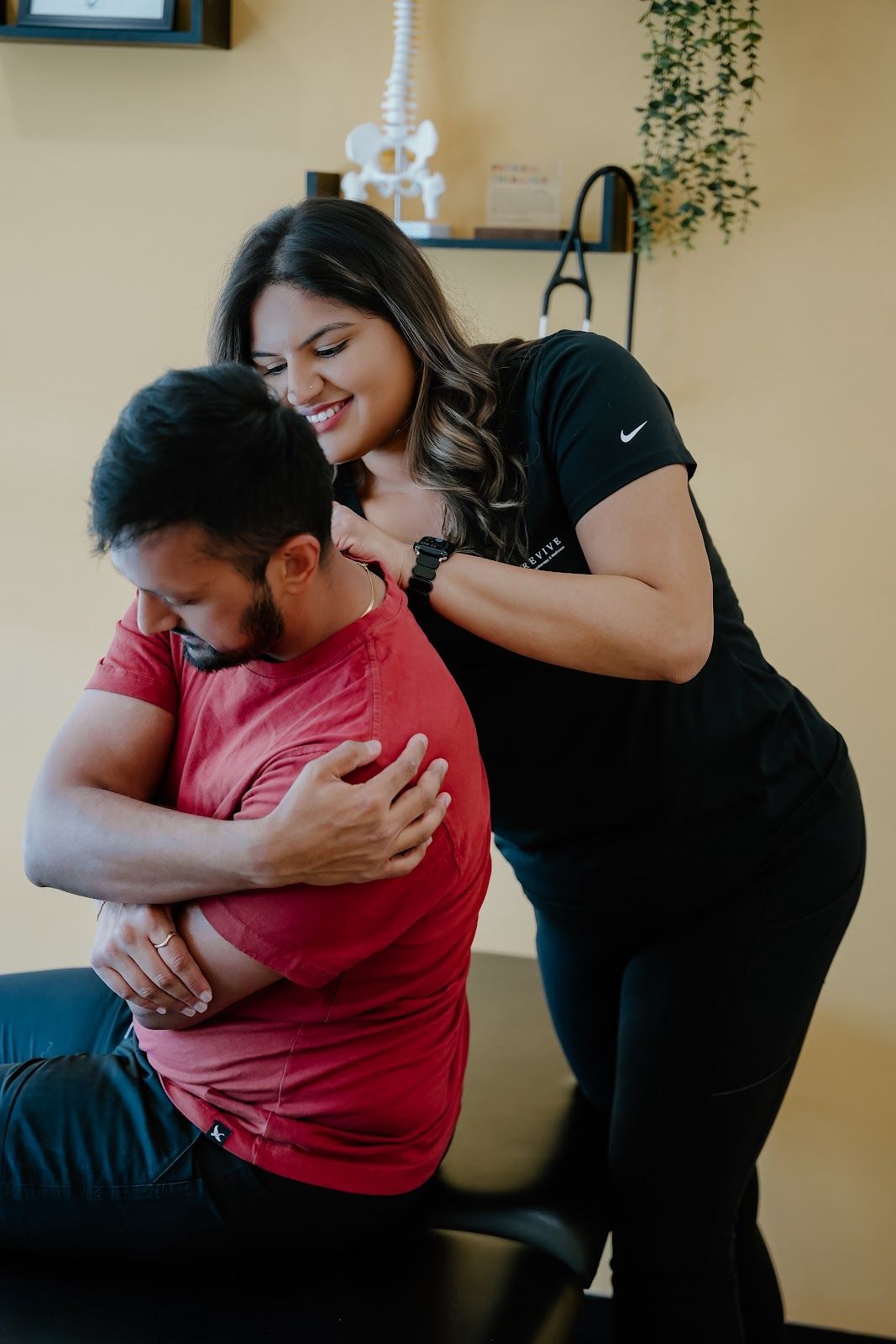 Chiropractor adjusting a patient's neck, smiling. Office setting with skeleton model.