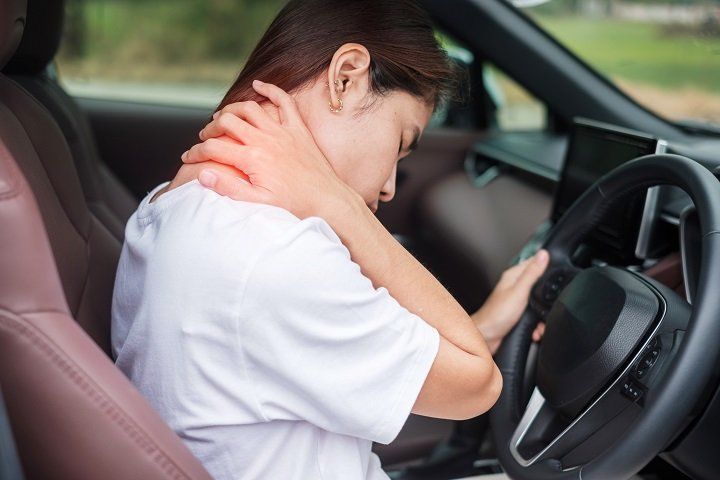 Woman in car clutching neck, indicating pain, likely suffering from an injury.