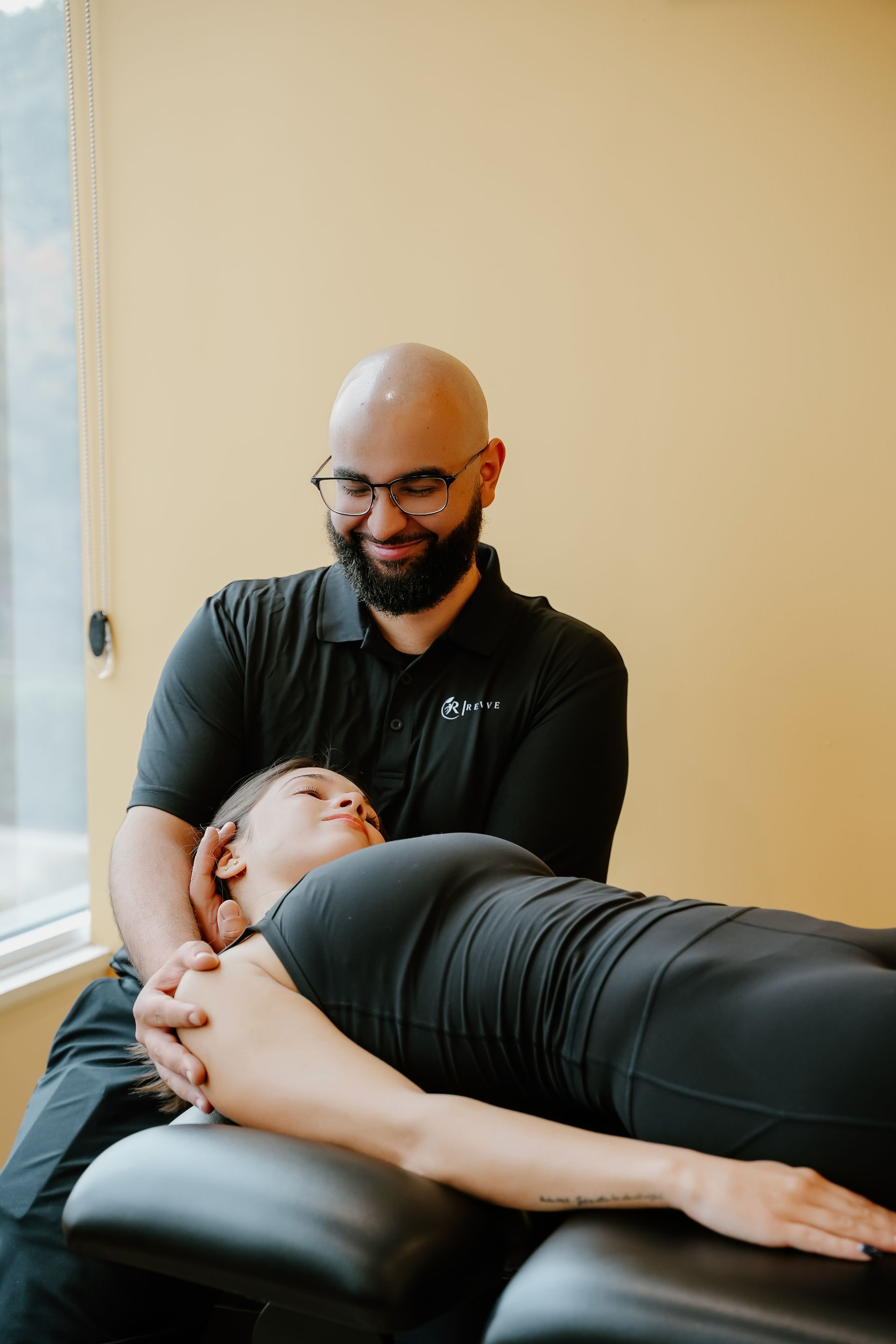 A person receiving physical therapy from a smiling therapist. Inside a room, the patient lies on a table.