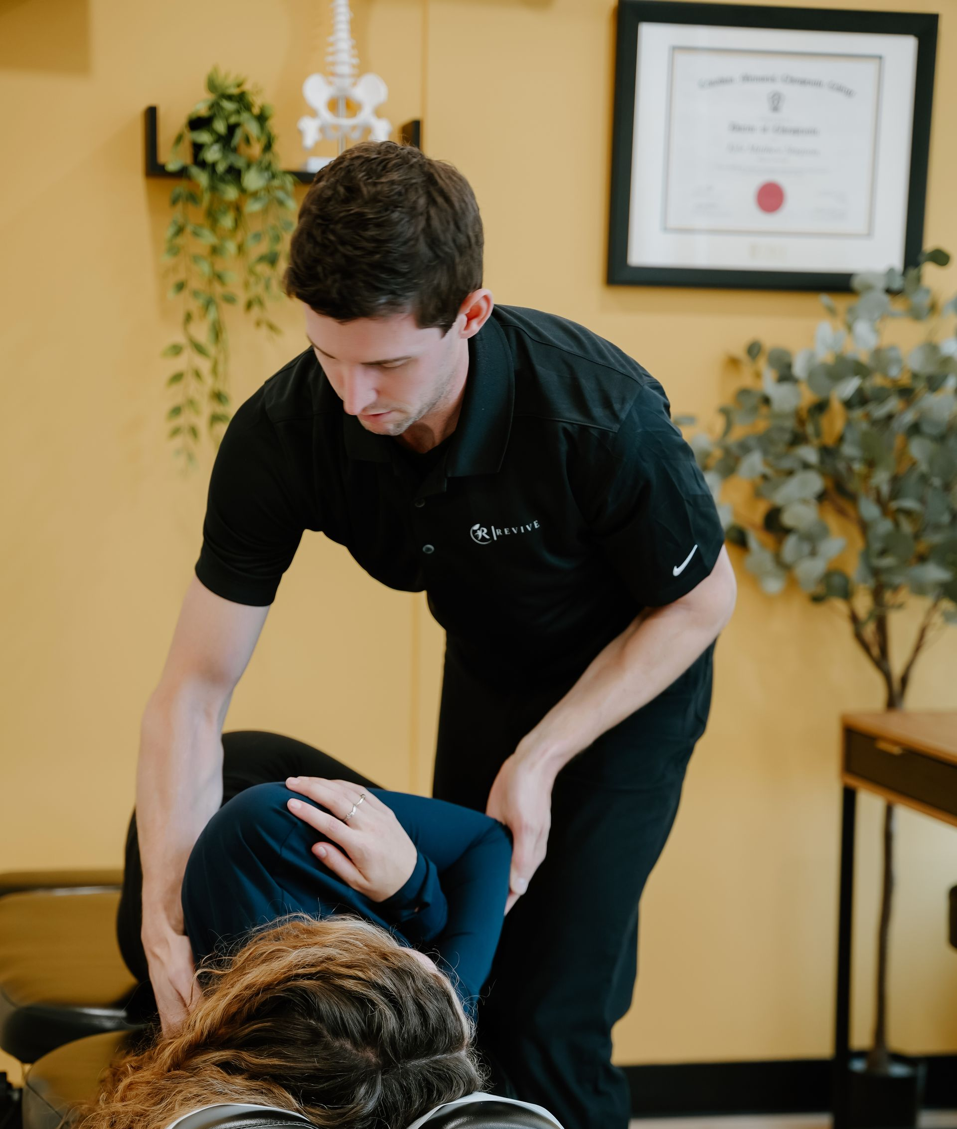 Man holding his neck, likely in pain, in front of a white wall and shelves.