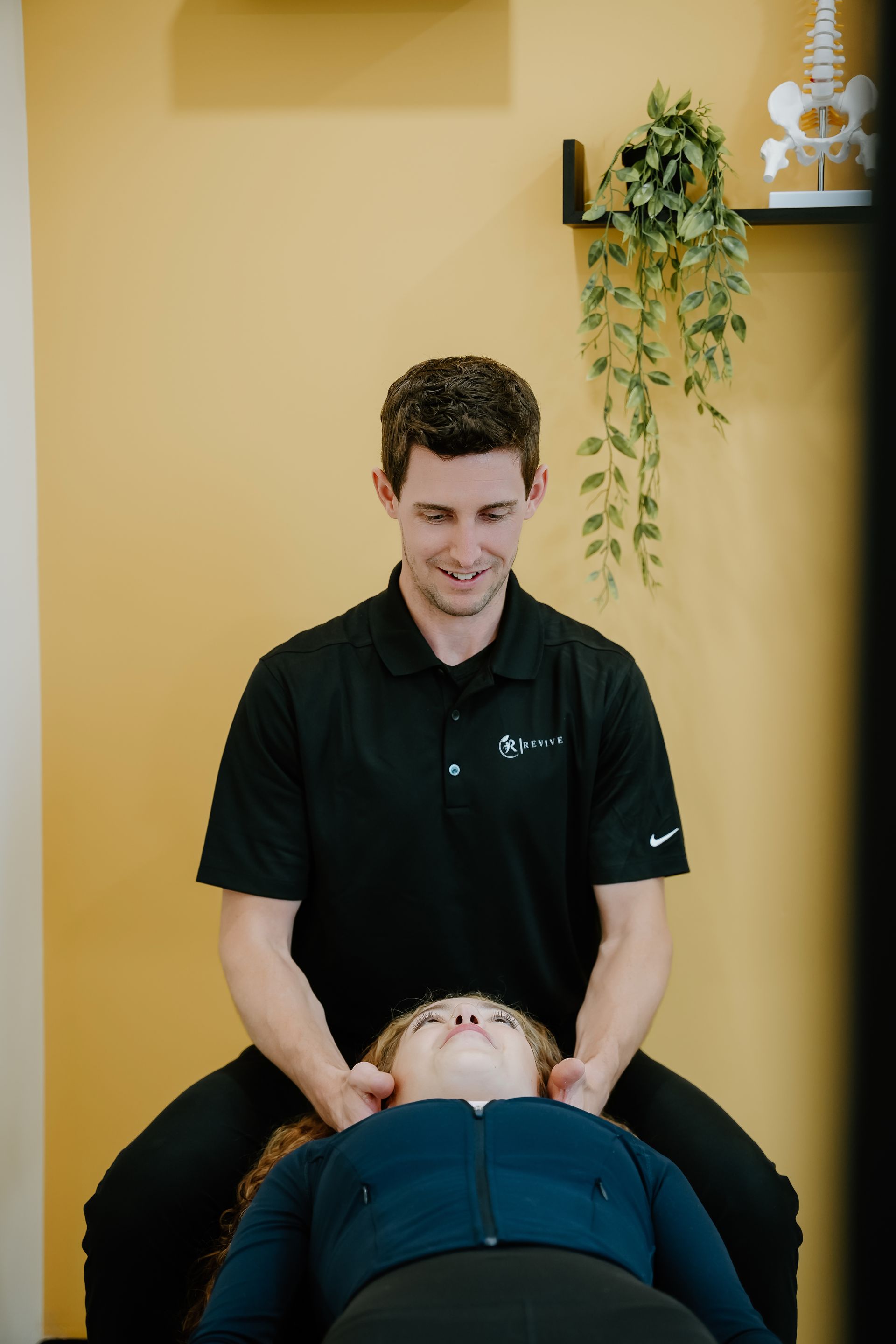 A man in black shirt performing neck massage on a person seated on a chair, indoors.