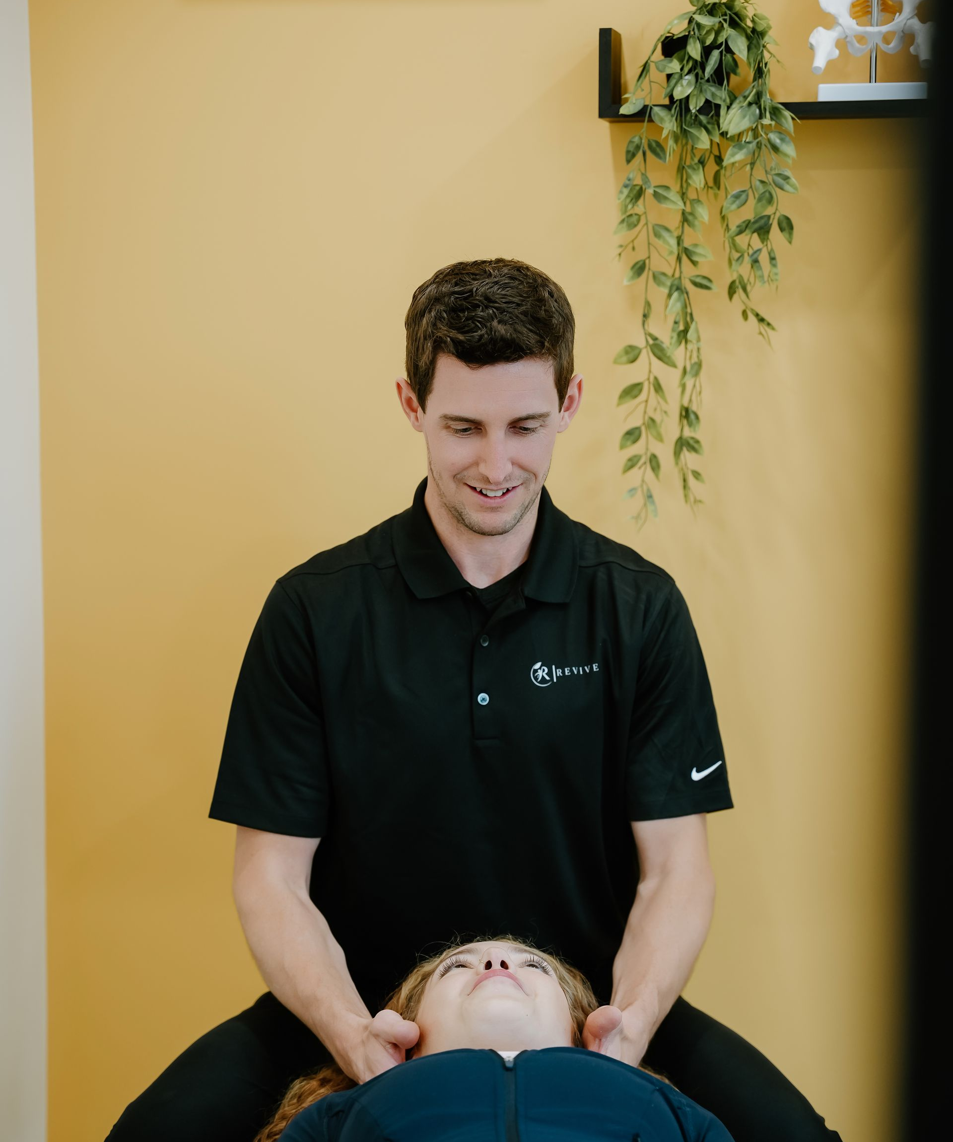 A man in black shirt performing neck massage on a person seated on a chair, indoors.