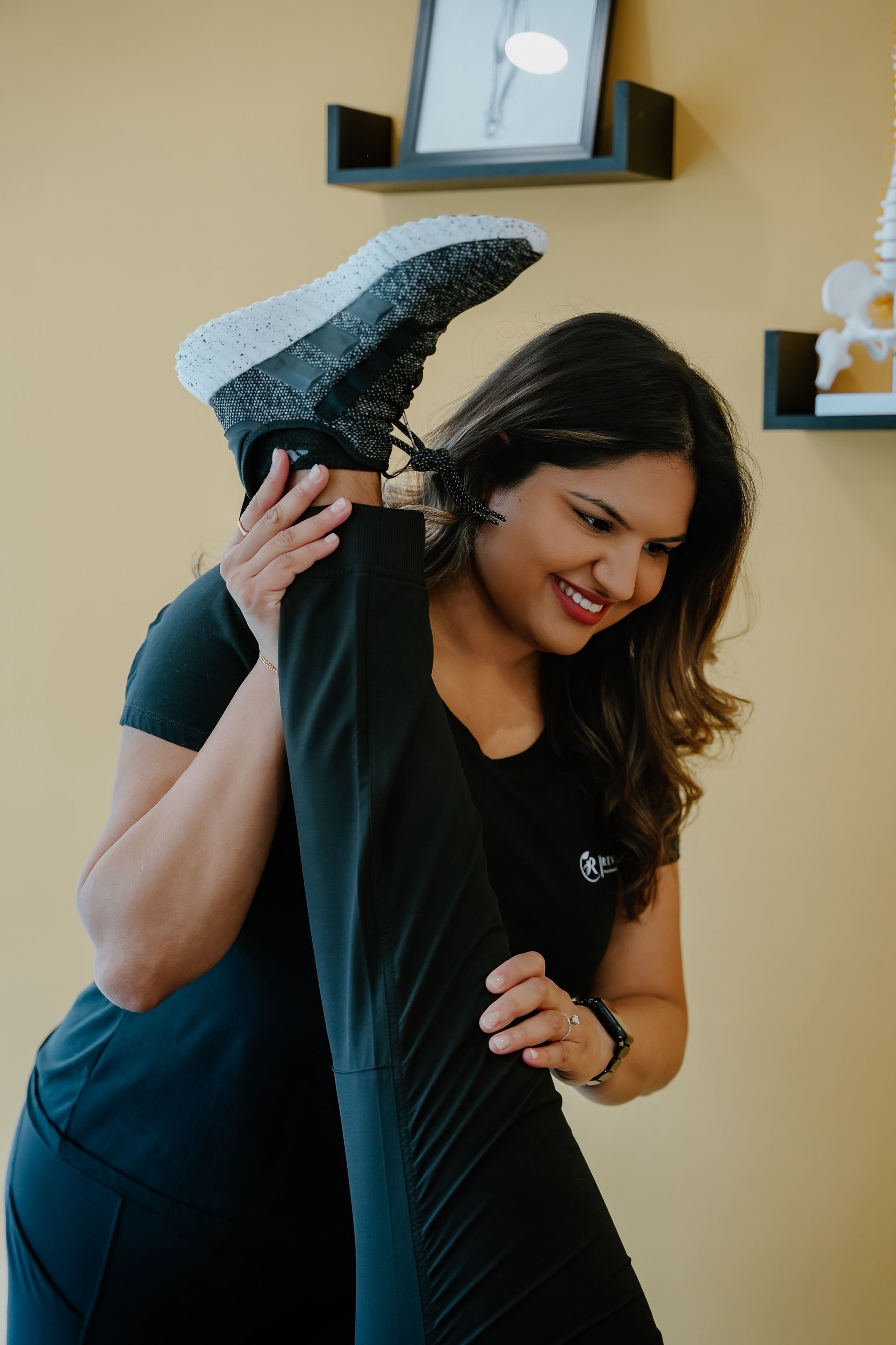 Woman stretches a leg toward the ceiling. She smiles in a yellow-walled room with a small framed artwork.