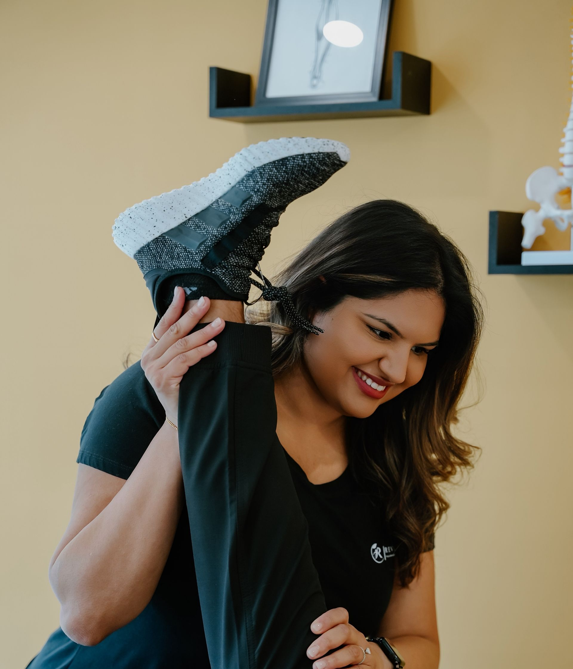 Woman stretches a leg toward the ceiling. She smiles in a yellow-walled room with a small framed artwork.