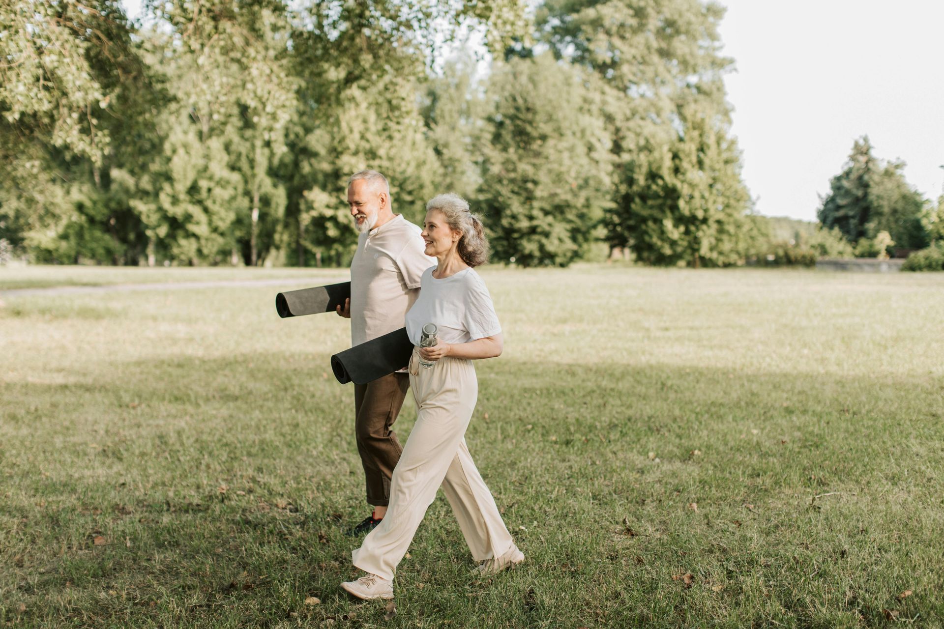 Couple walking in a sunny park, carrying yoga mats.