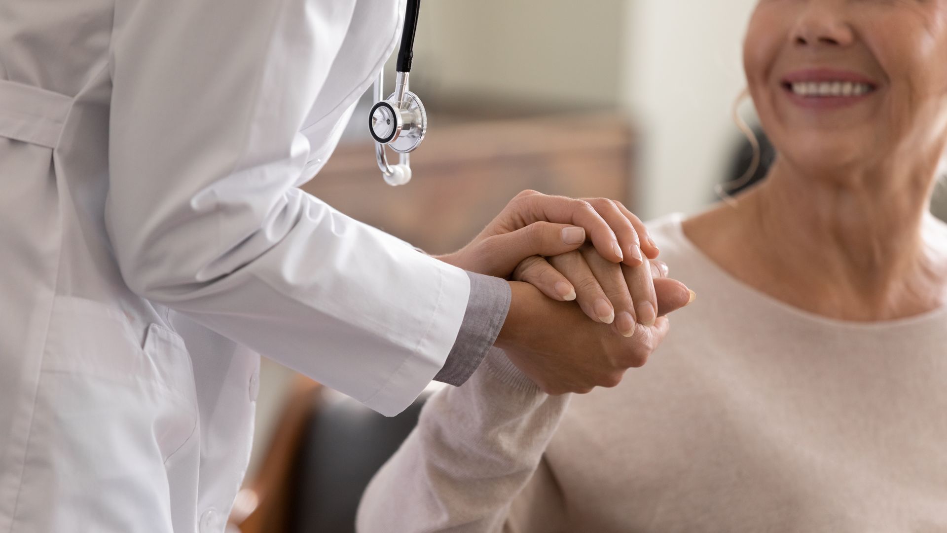 Doctor holding a patient's hands, offering support. Smiling patient, white coat, stethoscope.