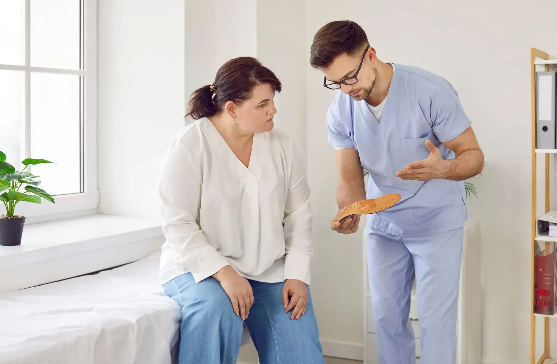 Doctor explaining a foot orthotic to a patient in a light-filled exam room.