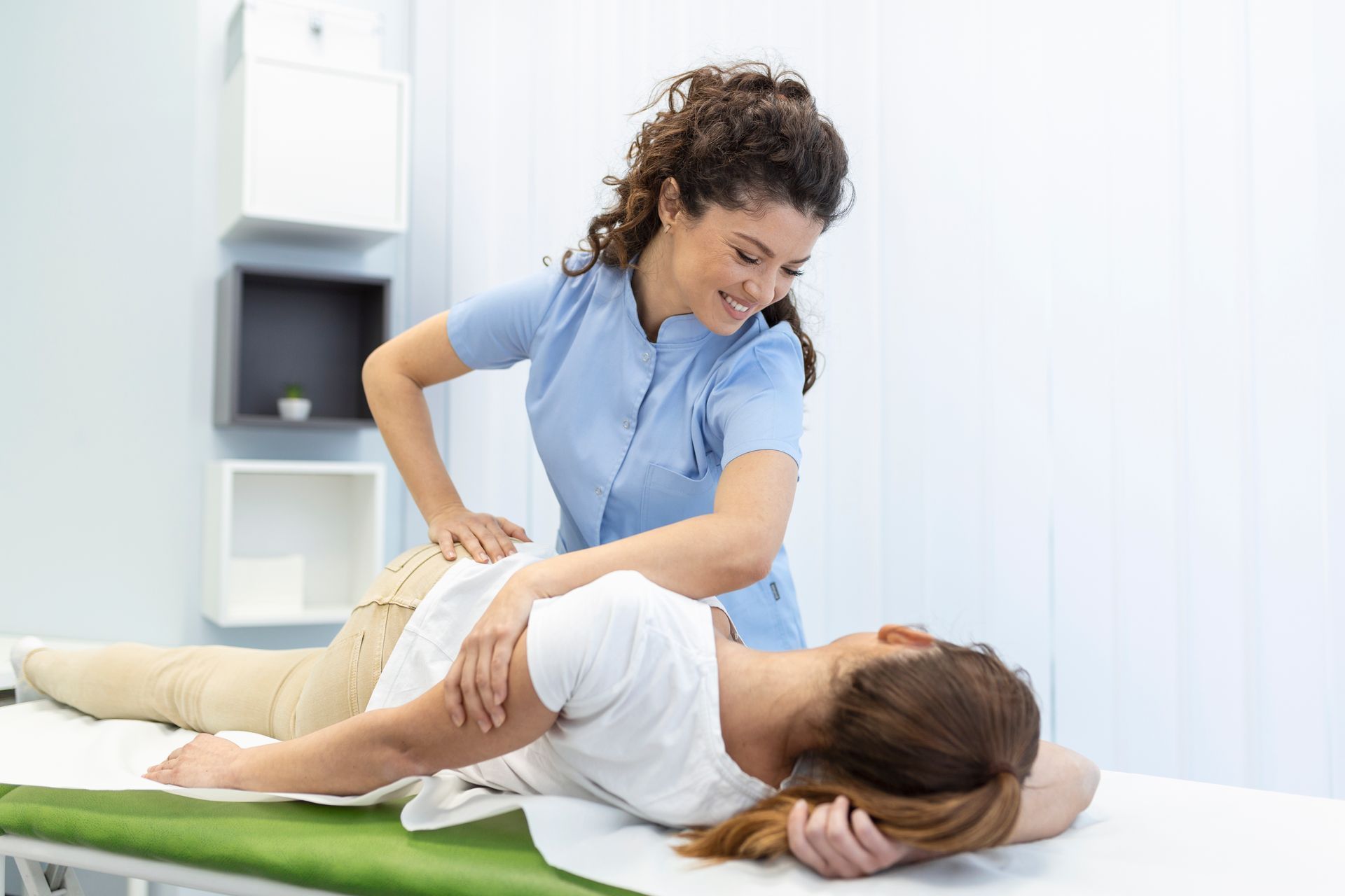 Medical professional doing physical therapy on a patient's back; light blue scrubs; smiling; lying on a medical table.