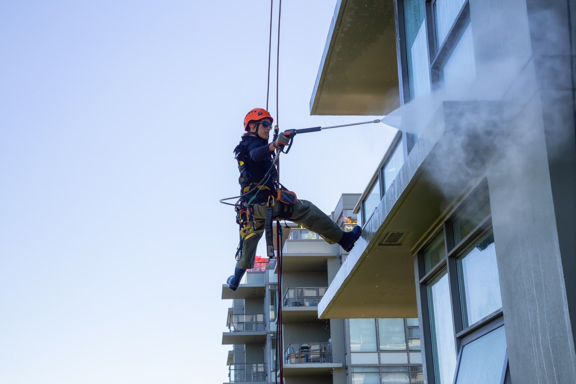 A man is cleaning the side of a building with a high pressure washer.
