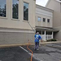 A man is cleaning the windows of a building with a hose.