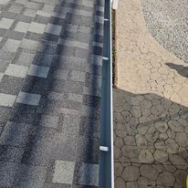 A close up of a gutter on a roof next to a sidewalk.