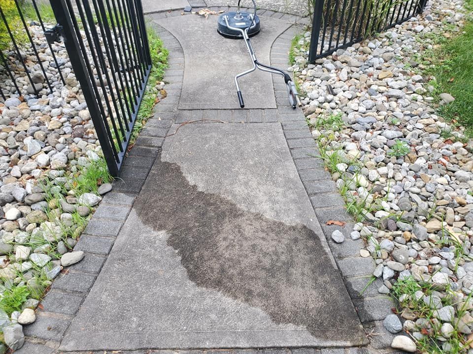 A before image of a dirty concrete walkway next to a gate and rocks.