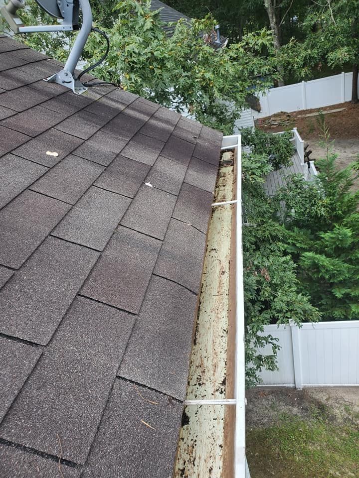 A gutter on the roof of a house with a white fence in the background.