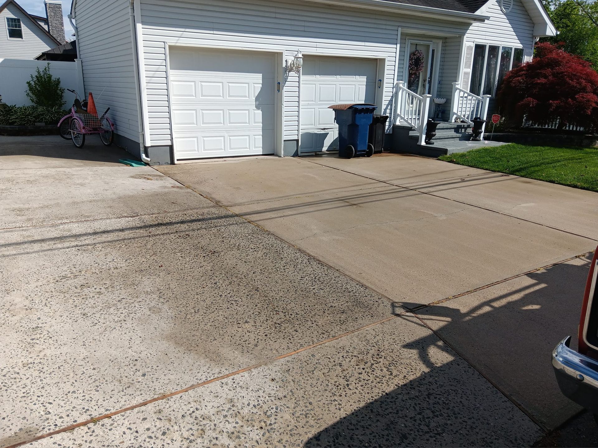 A car is parked in front of a house with two garage doors.