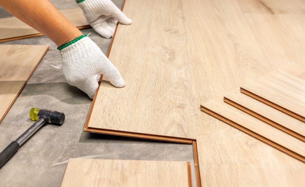 Person in gloves installing light wood flooring, indoors.