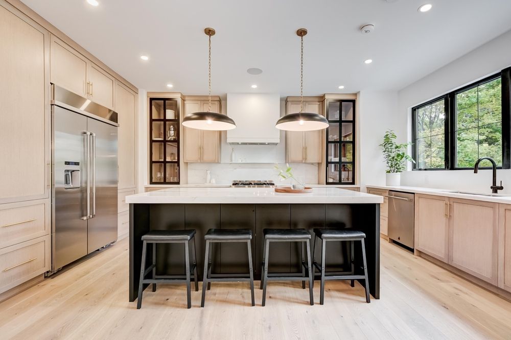 Modern kitchen with island and stools, stainless steel appliances, and light wood cabinets.