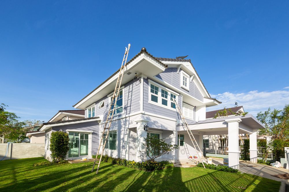 Two-story blue and white house with a ladder against the side, on a sunny day.