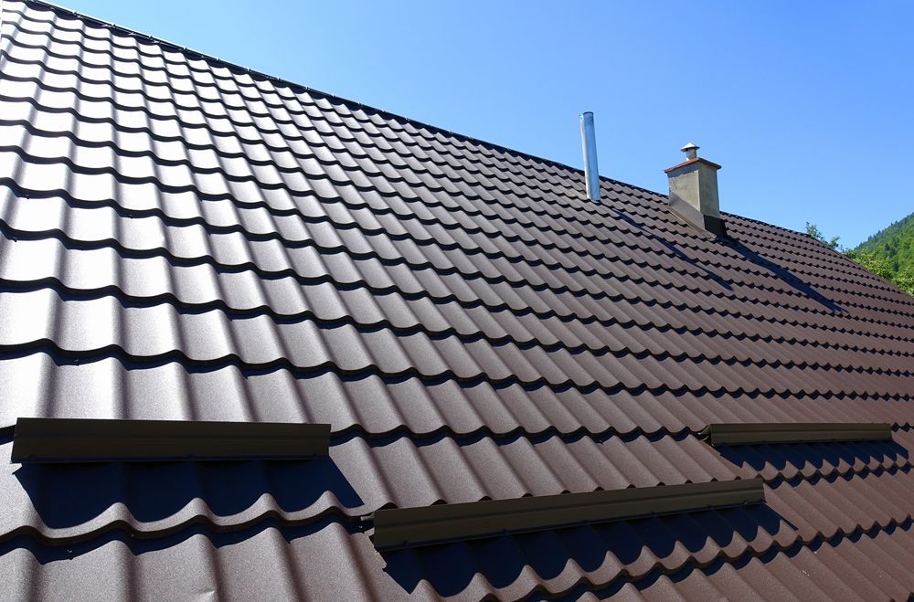 Brown metal roof with a chimney and skylights on a sunny day.
