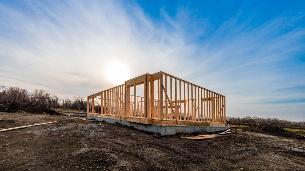 Framing of a new house under construction against a blue sky with a bright sun.