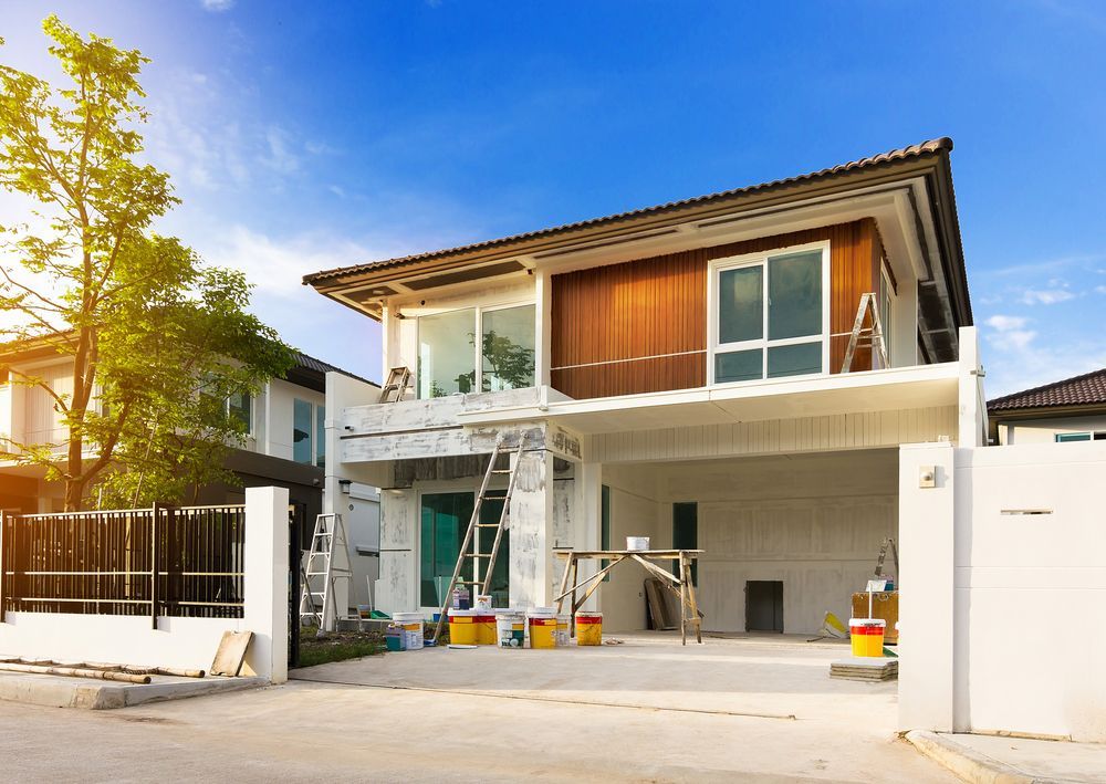 House under construction with paint buckets and ladders, under a bright blue sky.