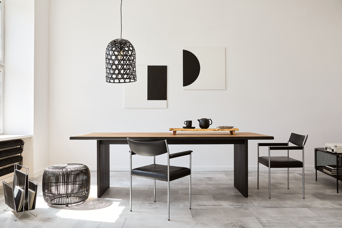 Dining room with long wooden table, black chairs, and abstract art on white wall.