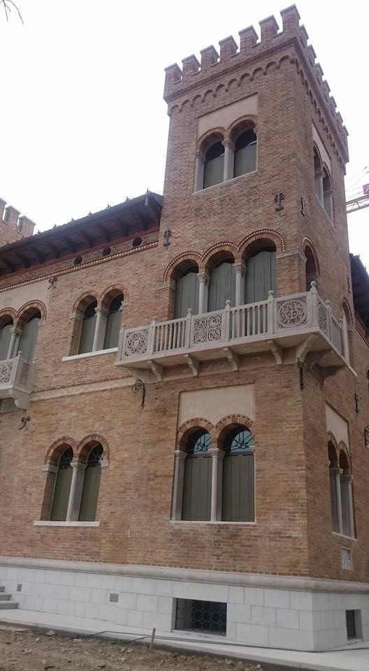 Edificio in mattoni con un'alta torre e un balcone. Le finestre hanno la sommità arcuata. Ripresa esterna.