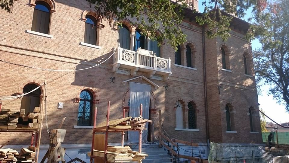 Edificio in mattoni con finestre ad arco, piccolo balcone e impalcature edili.