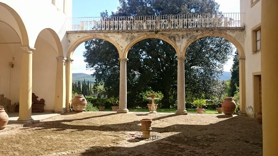 Cortile con archi, pilastri e un balcone che si affaccia sul giardino nelle giornate di sole.