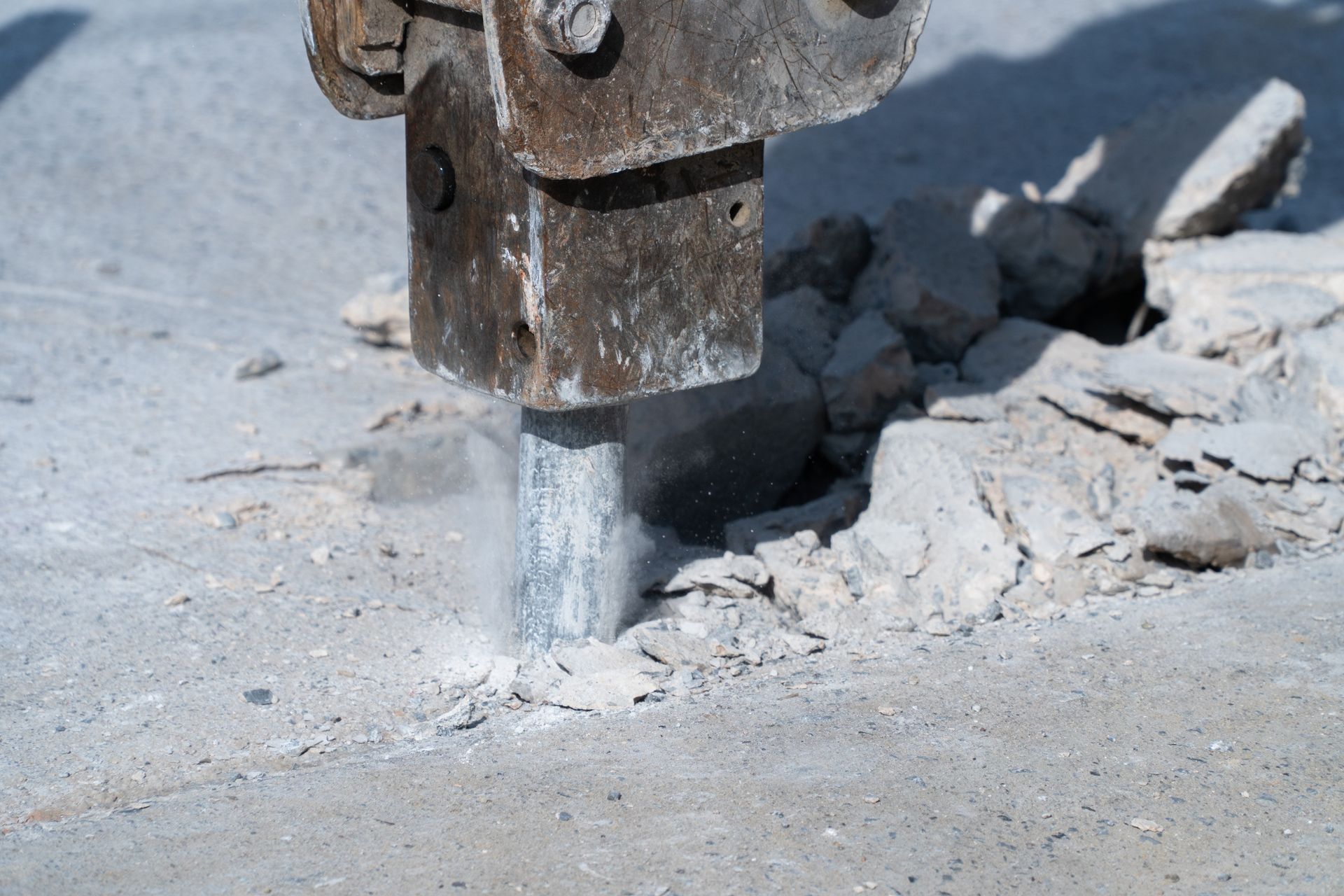 A close-up of a hydraulic jackhammer being drilled into a cement road. A close-up of a hydraulic jackhammer being drilled into a cement road.