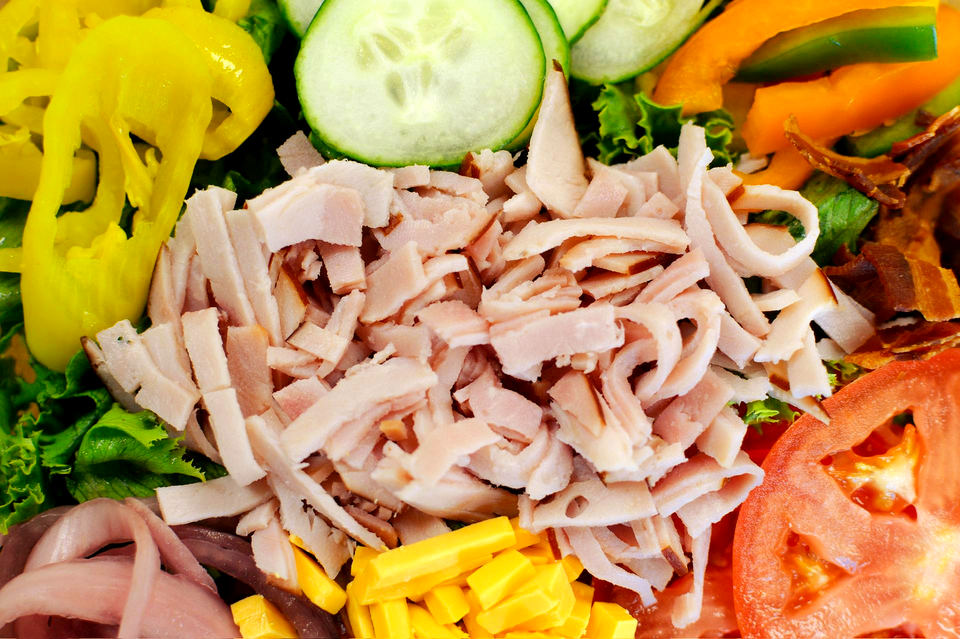 Ciabatta sandwich, cut in half, filled with lettuce, tomato, and what appears to be chicken. Served with a side salad.