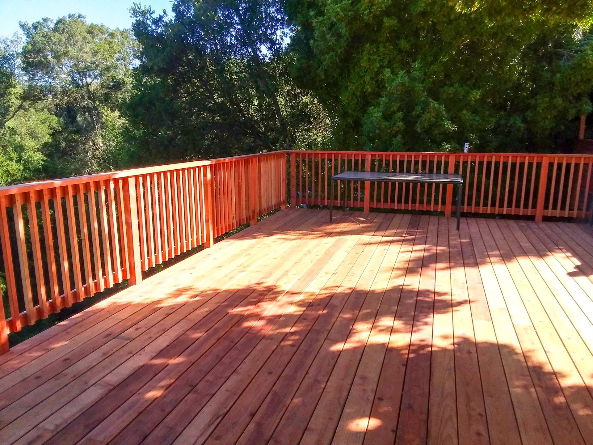Wooden deck with orange railing, a table, and trees in the background. Sunny day.