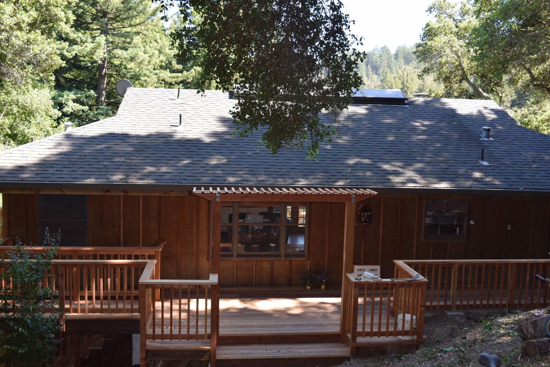 Wooden cabin with a deck, surrounded by trees.