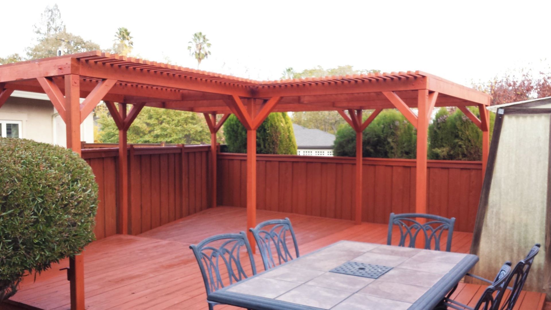 Red stained wooden deck with a matching pergola and outdoor dining set.