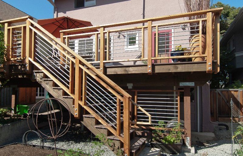 Wooden deck with staircase, metal railings, and attached to a light pink building.
