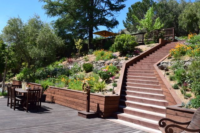 Wooden staircase and terraced garden with flowers, leading uphill to a shaded area.