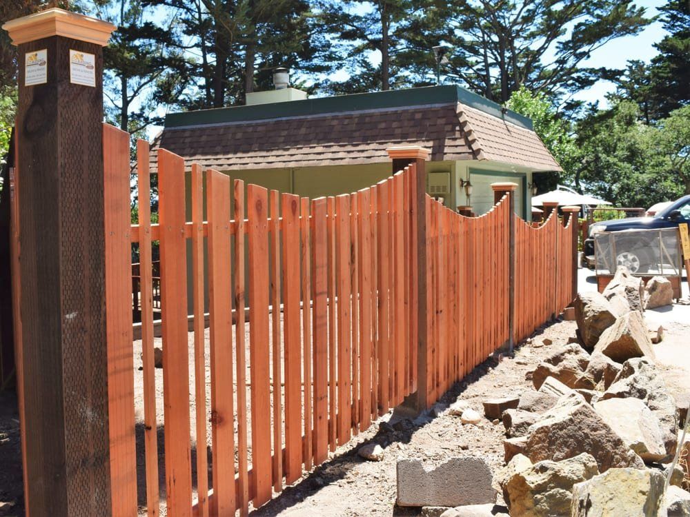 Wooden fence with a curved top, in front of a house.
