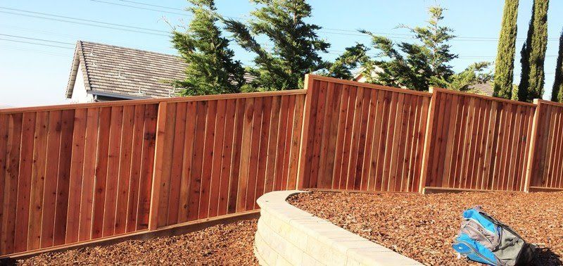 Wooden fence in a yard with a retaining wall and trees.