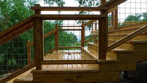 Wooden staircase with wire mesh railing overlooking a green landscape.