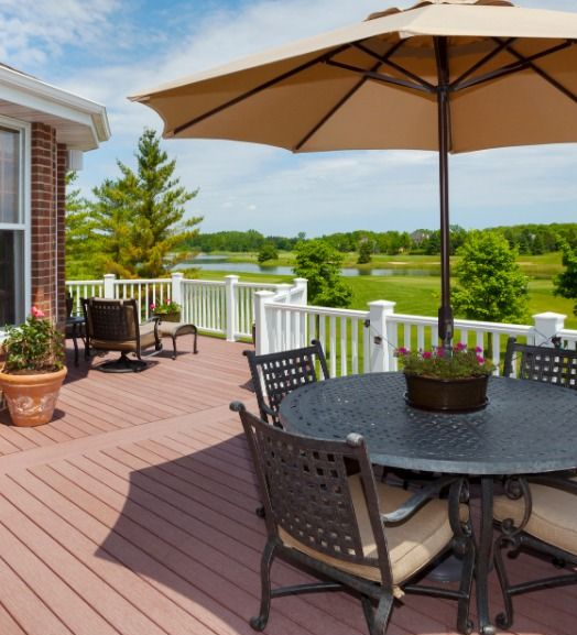 Patio with round table, umbrella, and chairs overlooking a scenic landscape with water.