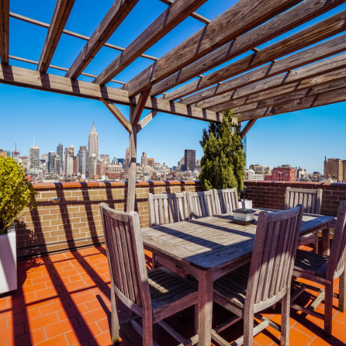 Outdoor dining set on a rooftop overlooking the New York City skyline, under a wooden pergola.