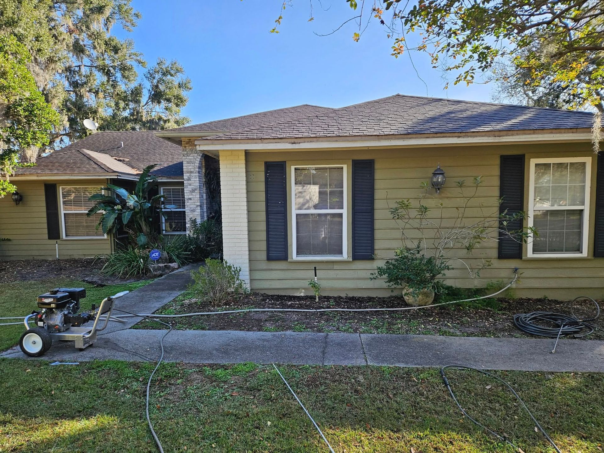 A house with green siding and black shutters. A power washer sits on the sidewalk.