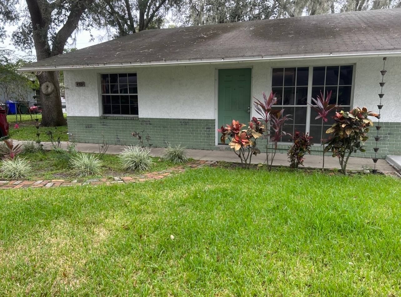 A one-story house with white and green siding, small lawn, and colorful plants in front.